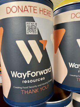 food donation barrel with WayForward Resources logo that reads DONATE HERE with a QR code, a large orange arrow and and stripes in navy, light blue and peach