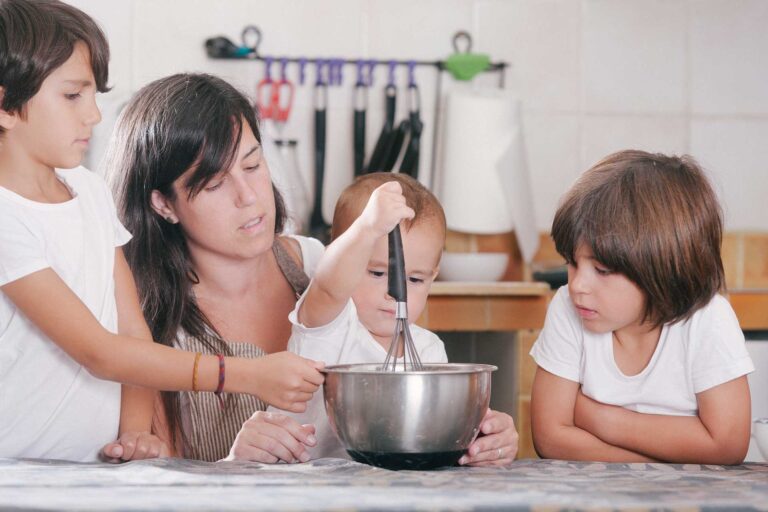 Mother with three young children stirring bowl in kitchen.