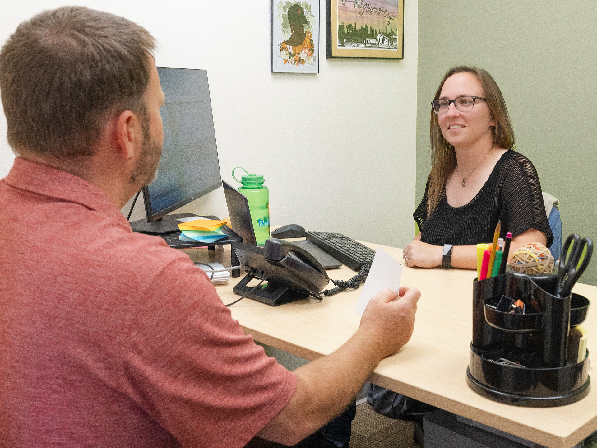 Two people sitting on opposite sides of a desk in an office talking.